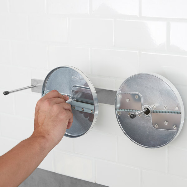 A hand using a tool to open a metal circular object on a wall.