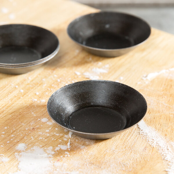A black Matfer Bourgeat quiche mold on a wood surface.