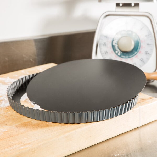 A Matfer Bourgeat fluted non-stick tart pan with removable bottom on a wooden surface.