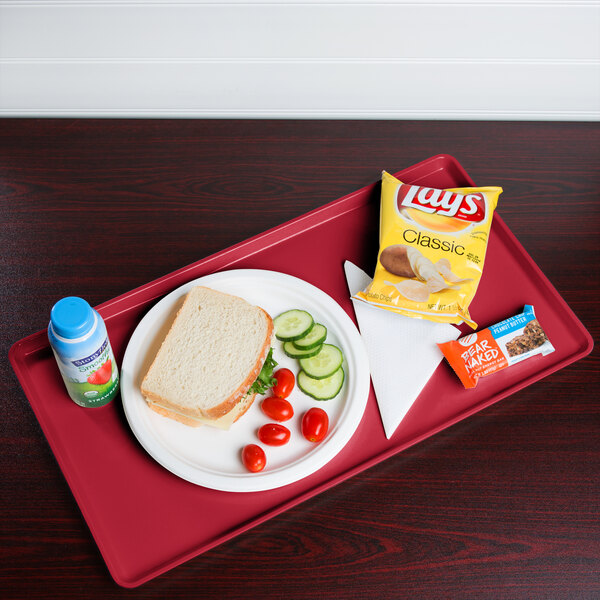 A Cambro signal red dietary tray with a sandwich, chips, and a drink on it.