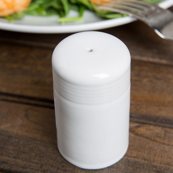 A Tuxton white china salt shaker on a table.