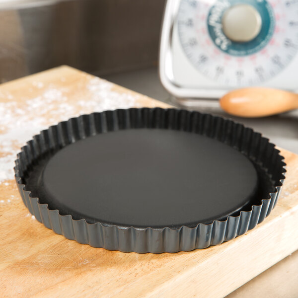 A Matfer Bourgeat fluted tart pan with a raised bottom filled with a black fruit tart on a wooden surface.