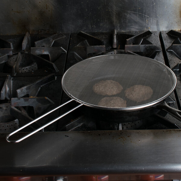 A Lodge splatter screen over a pan with meat patties cooking on a stove.