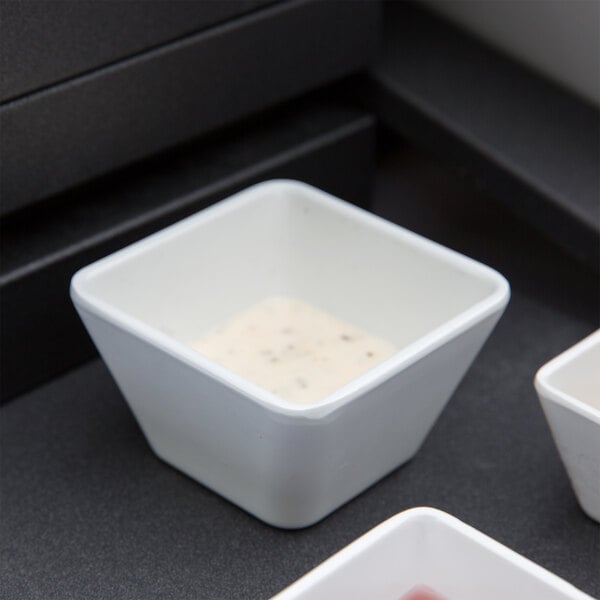 A white square Vollrath melamine bowl with liquid in it.