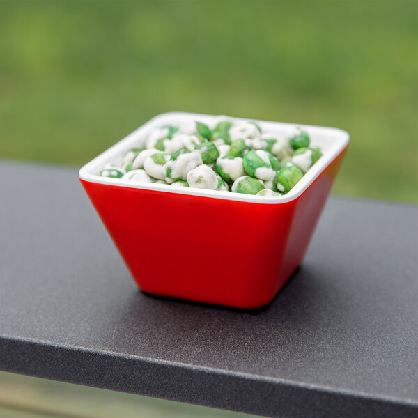 A red Vollrath melamine bowl with green and white food in it on a table.