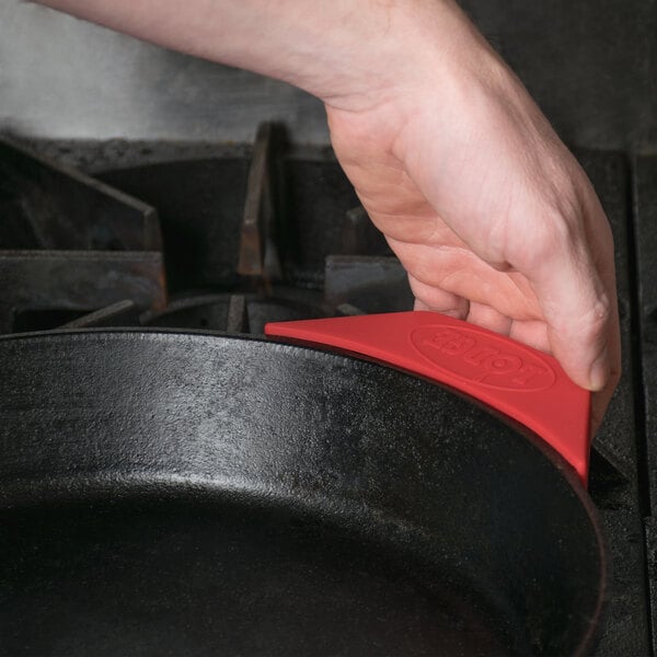 A person using a Lodge red silicone assist handle holder to hold a red spatula over a black pan.