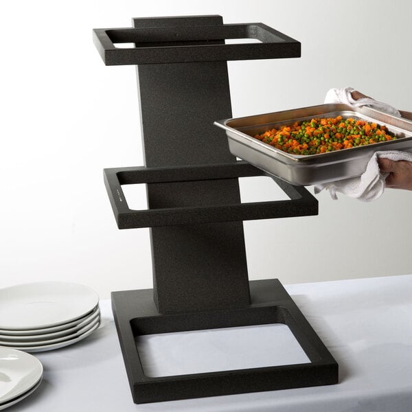 A person holding a Vollrath black wood tiered stand with food pans.