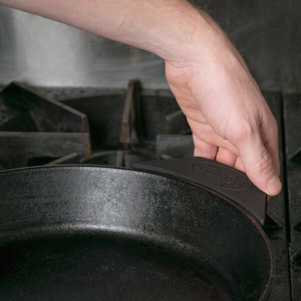A person using a black Lodge silicone handle holder on a black cast iron pan.