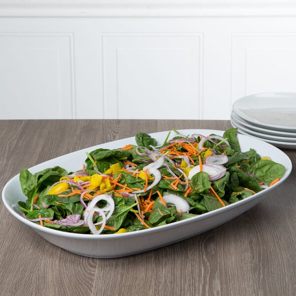 An oblong white melamine bowl filled with salad on a table.