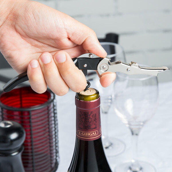 A hand using a Pullparrot waiter's corkscrew with a black and silver handle to open a wine bottle.