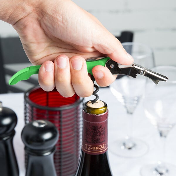 A hand holding Pulltap's Original Waiter's Corkscrew with a lime green handle opening a bottle of wine.
