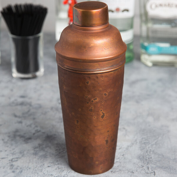An American Metalcraft hammered antique copper cobbler cocktail shaker on a counter.