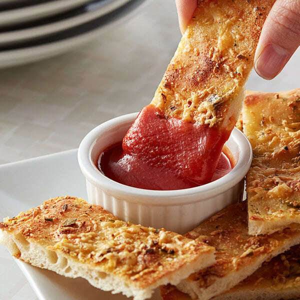 A hand dipping a piece of bread into a bowl of Furmano's tomato sauce.