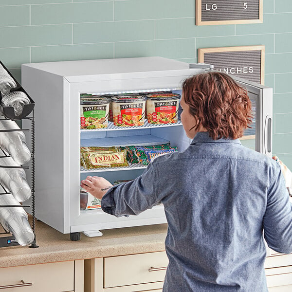 A woman opening an Avantco white countertop display freezer with a swing door.