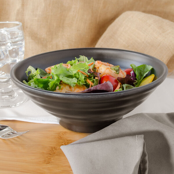 A black matte melamine bowl filled with salad with shrimp and tomatoes.