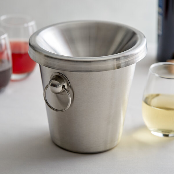 A Franmara customizable stainless steel wine tasting spittoon on a counter next to a glass of white wine.