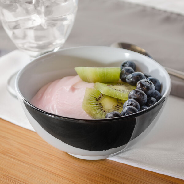 A white GET melamine bowl filled with yogurt, kiwi, and blueberries with a spoon.