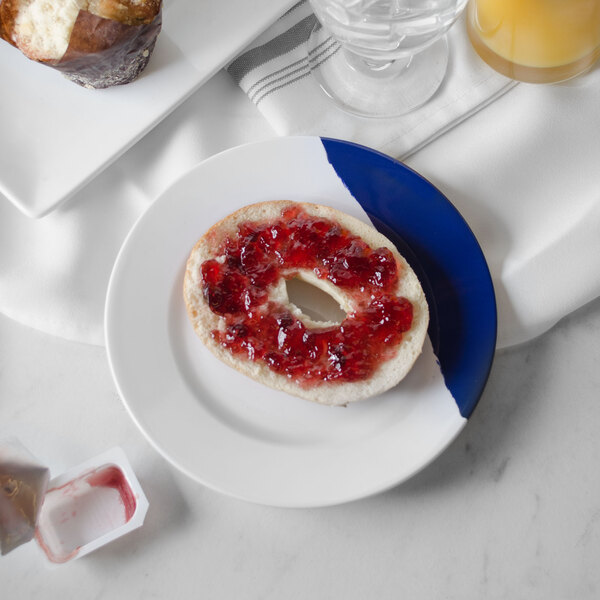 A white and navy blue wide rim round melamine plate with a bagel and jam on it.