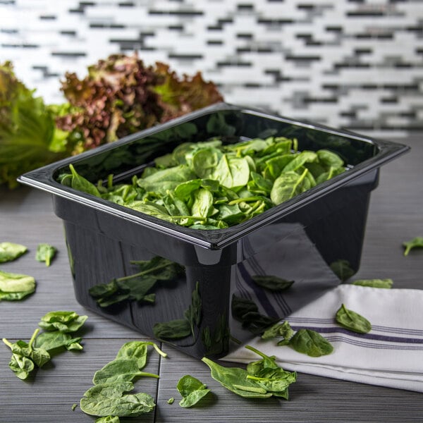 A Carlisle black plastic food pan filled with spinach on a counter.
