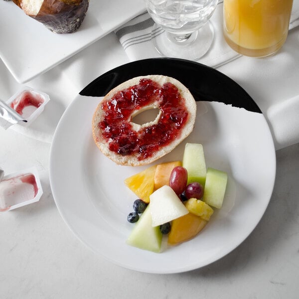 A GET white melamine plate with a black rim holding a bagel with jam and a plate of fruit.