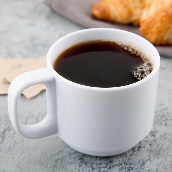 A white stackable Tritan mug filled with coffee on a table with croissants.