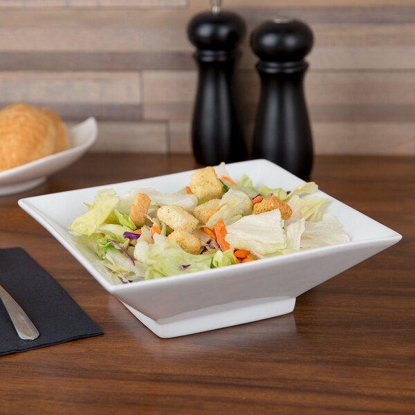 A CAC Citysquare white porcelain bowl filled with salad on a table.