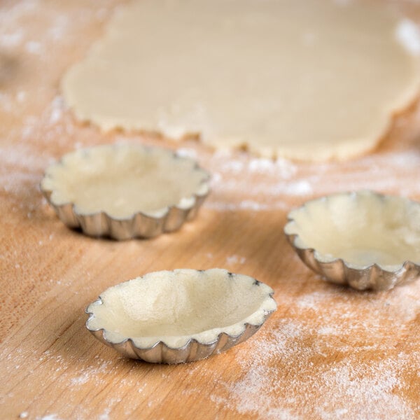 A wooden surface with small tarts made with Ateco petit four molds and dough.
