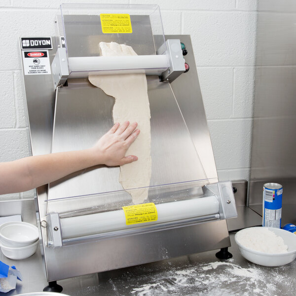 A person using a Doyon Countertop Dough Sheeter to roll pizza dough.