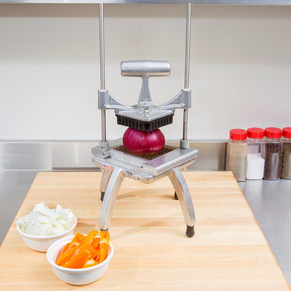 A Nemco Easy Chopper II sits on a professional kitchen counter with orange peppers, red onions, and other vegetables.