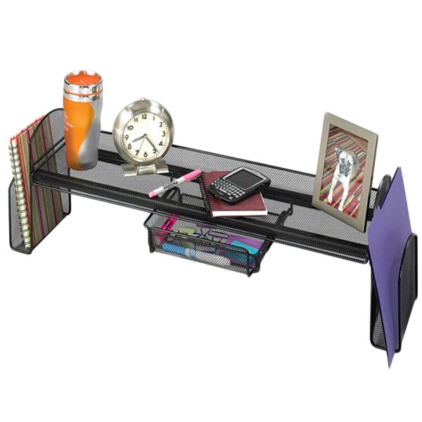 A Safco Onyx steel mesh off-surface shelf on a desk with a clock and other objects on it.