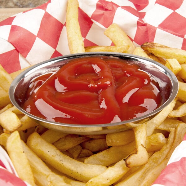 A stainless steel oval sauce cup of ketchup next to french fries.