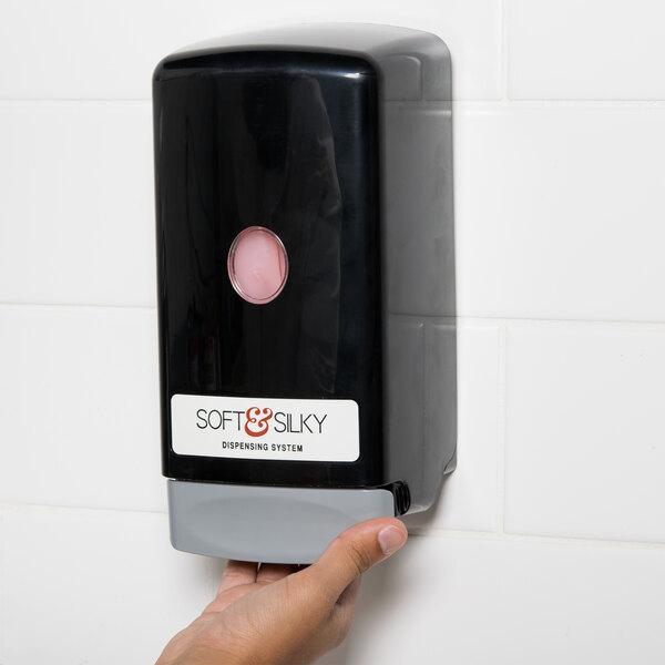 A person's hand holding a Kutol black bag-in-box hand soap dispenser.
