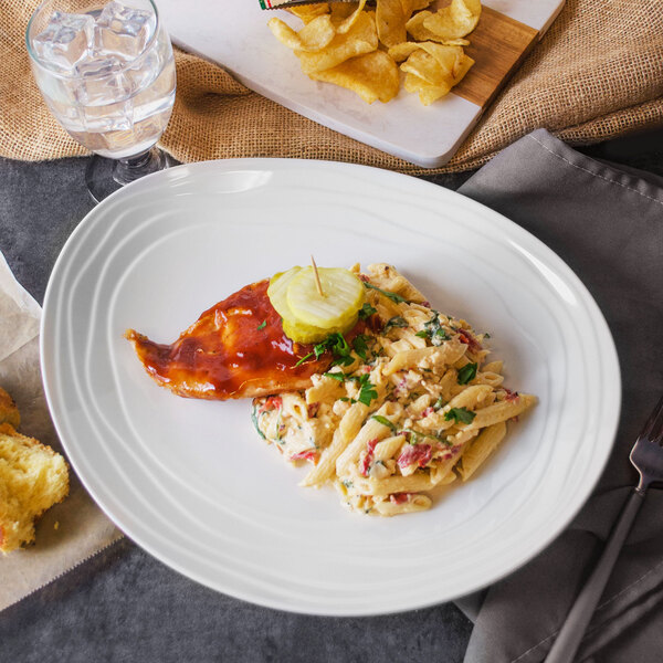 A Magnolia melamine oval platter with a plate of pasta and a fork on a table.