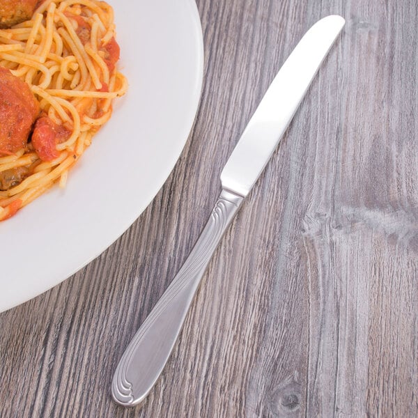 A silver Oneida Scroll dinner knife on a plate of spaghetti with sauce.