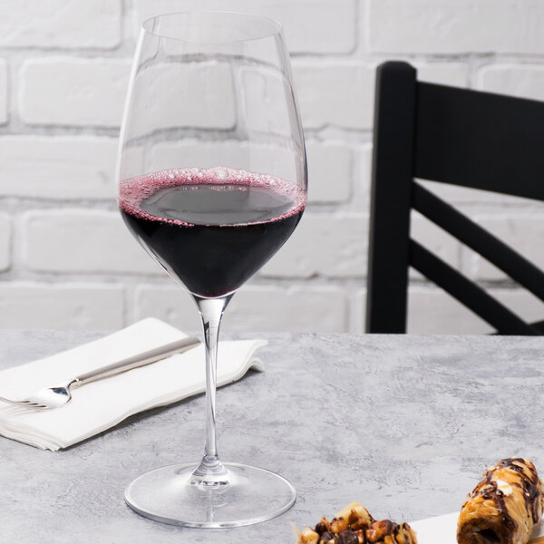 A Spiegelau Bordeaux wine glass filled with red wine on a table.