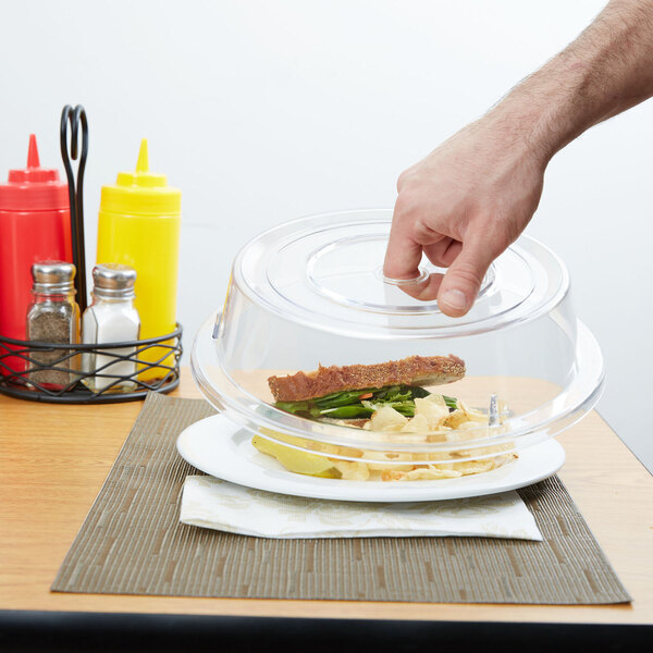 A hand reaching for a sandwich on a clear plate.