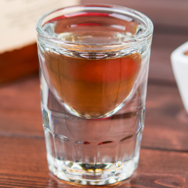 A Libbey fluted shot glass with brown liquid on a table.