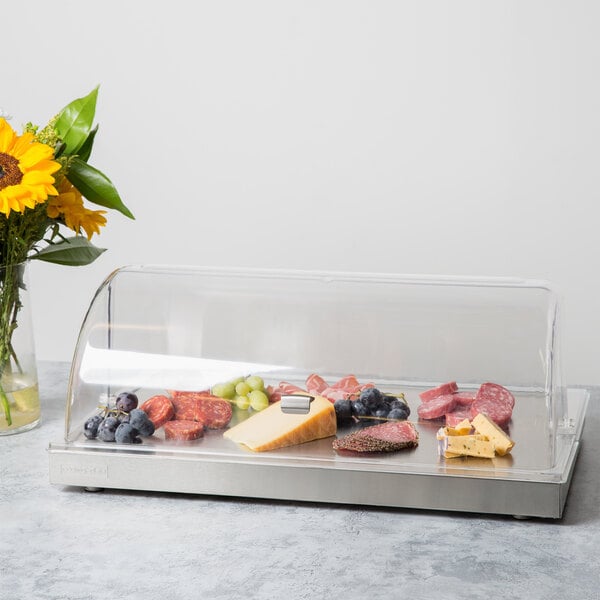 A Vollrath stainless steel cooling plate with clear lid holding a variety of food on a counter.
