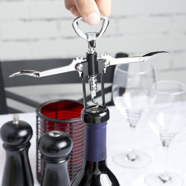 A hand using a Franmara Tavern Wing Corkscrew with a black body to open a bottle of wine.