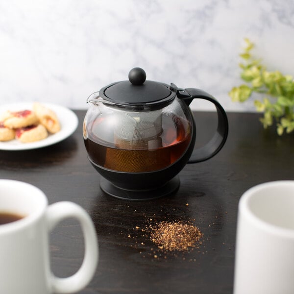 A Choice glass teapot with a stainless steel infuser and a cup of tea on a table.