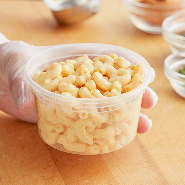 A hand holding a ChoiceHD translucent plastic deli container of macaroni and cheese.
