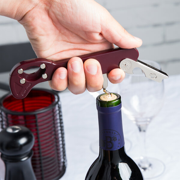 A person using a Franmara Boomerang Waiter's Corkscrew to open a wine bottle.