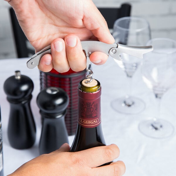 A person using a Franmara stainless steel corkscrew to open a bottle of wine.