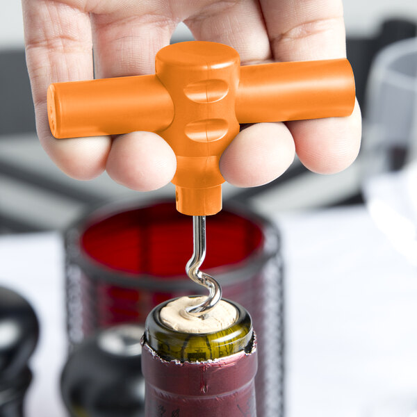 A hand using a Franmara orange plastic pocket corkscrew to open a wine bottle with a cork.
