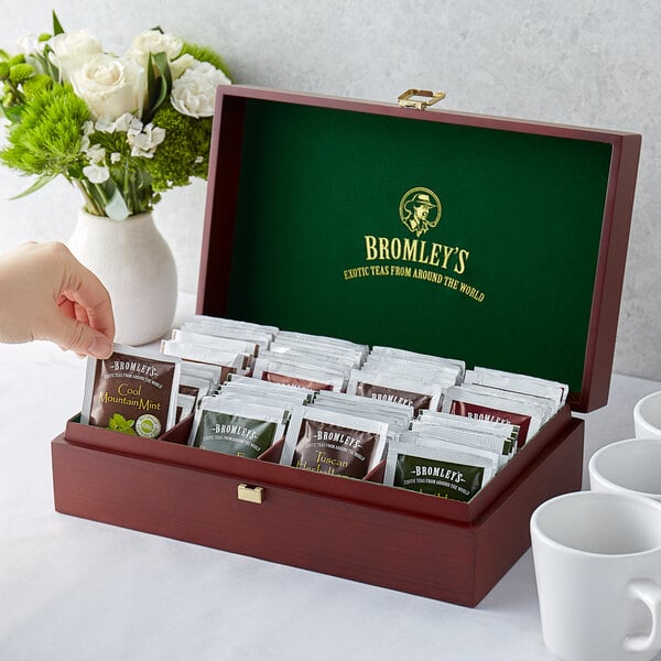 A hand holding a wooden Bromley tea chest with tea bags inside.
