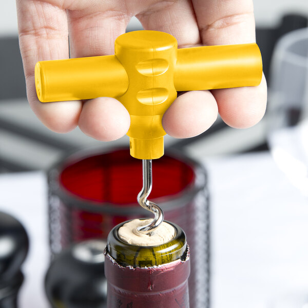 A hand holding a Franmara Lemon yellow plastic pocket corkscrew opening a wine bottle.