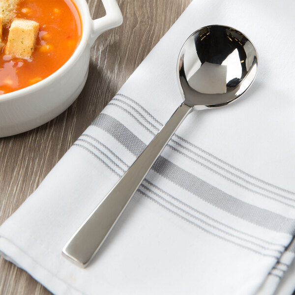 A Bon Chef rounded bowl soup spoon on a napkin next to a bowl of soup.
