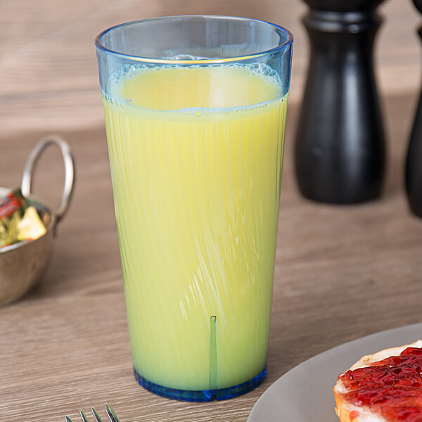 A Thunder Group blue polycarbonate tumbler filled with yellow liquid on a table next to a plate of food.