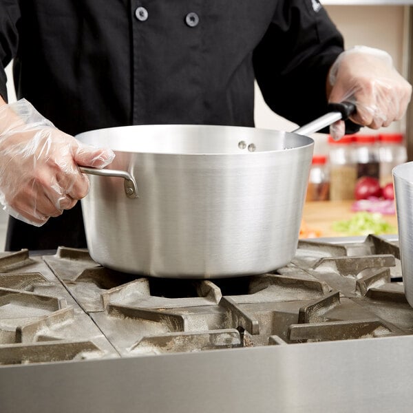 A chef holding a Vollrath Wear-Ever sauce pan with a black handle.