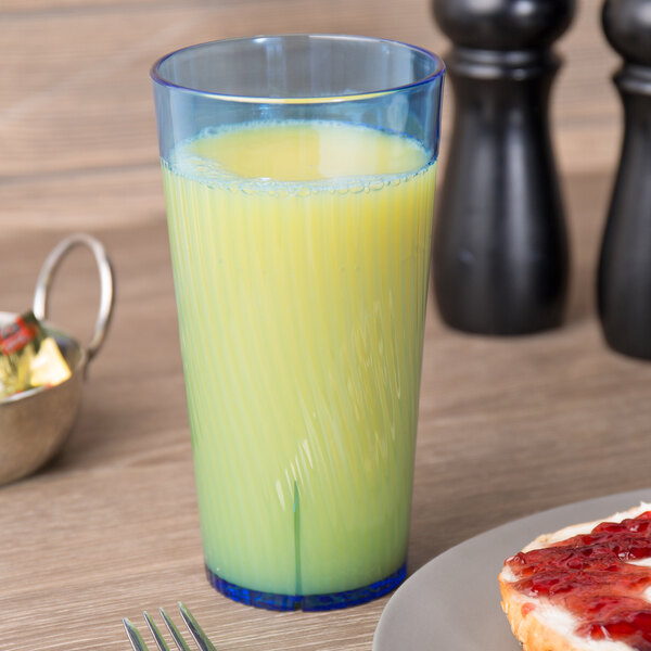 A Thunder Group blue polycarbonate tumbler filled with yellow juice on a table with a plate of food.